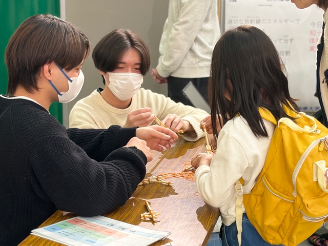 ボランティアサークルの学生が子どもに木の工作体験を教える様子